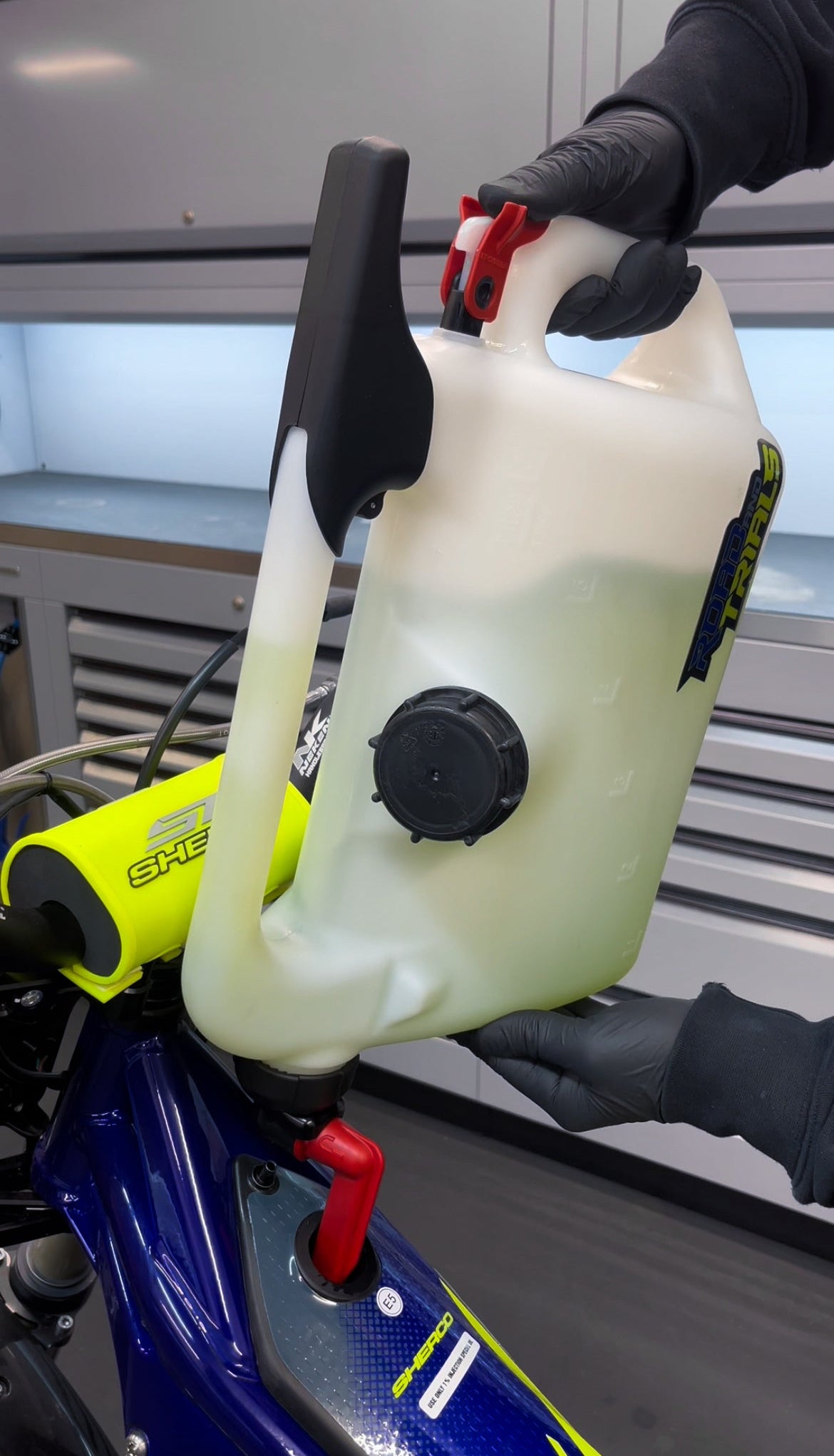 Mechanic holding a petrol fuel can container attached to a motorcycle in a workshop setting trials bike, motocross bike, enduro bike, off road.